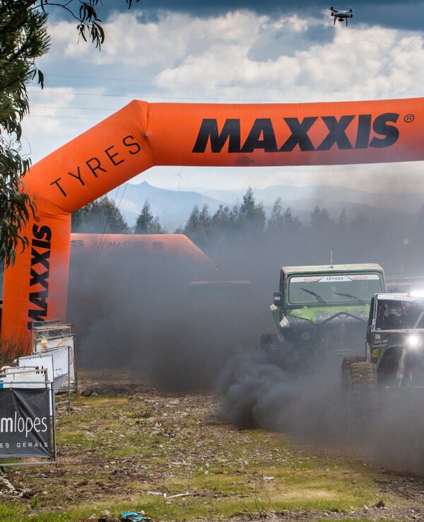 Veículos off-road a passar sob um arco publicitário da Maxxis, com fumo.
