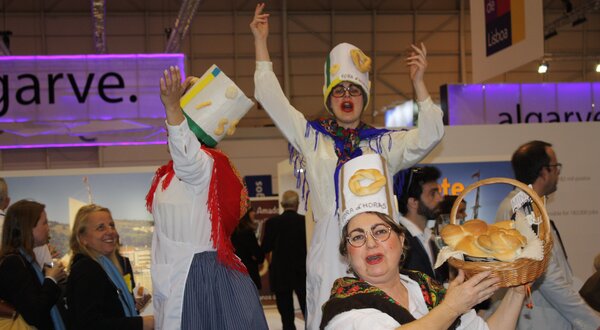 Grupo de pessoas vestidas com trajes tradicionais, a dançar e a segurar pão.