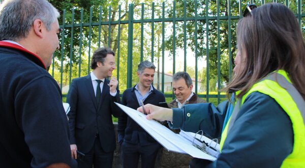 Grupo de pessoas a discutir, uma mulher com colete refletor a tomar notas.