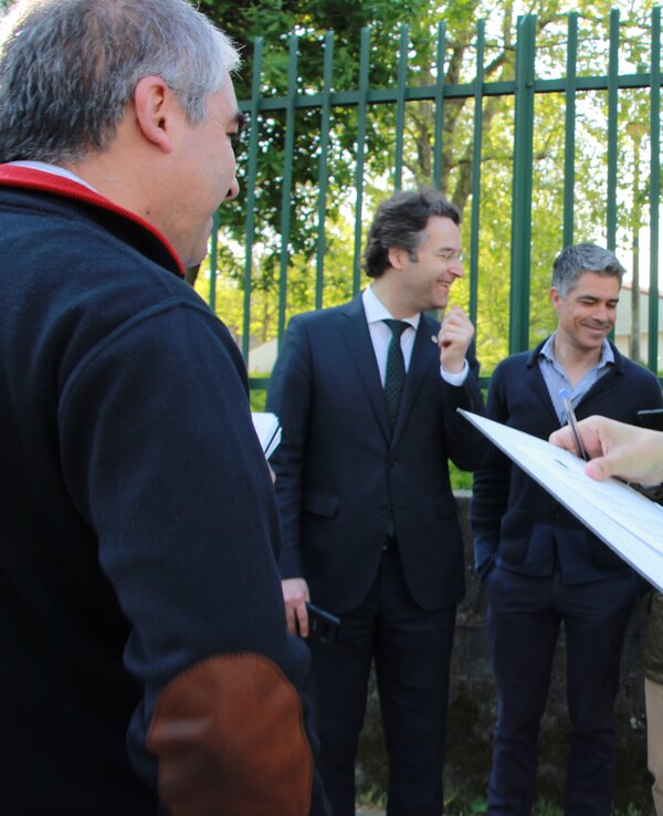 Grupo de pessoas a discutir, uma mulher com colete refletor a tomar notas.