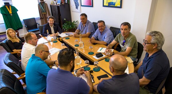 Grupo de homens e uma mulher reunidos à volta de uma mesa de reuniões.