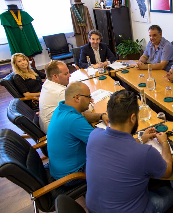 Grupo de homens e uma mulher reunidos à volta de uma mesa de reuniões.