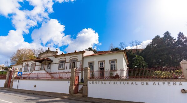 Fachada do Centro Cultural de Alfena, com céu azul e nuvens.