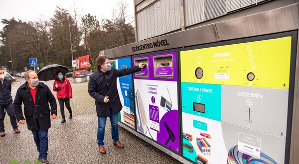 Homem a usar um ecoponto para reciclar, com pessoas ao fundo.