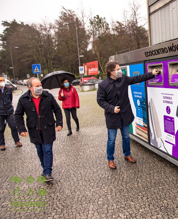 Homem a usar um ecoponto para reciclar, com pessoas ao fundo.