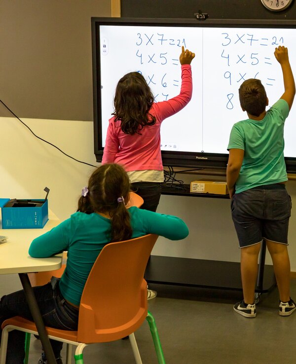 Duas crianças a resolver problemas de matemática num quadro interativo.