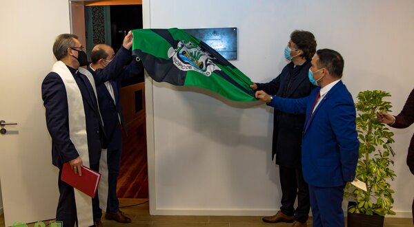 Cerimónia de descerramento de placa com bandeira em ambiente formal.