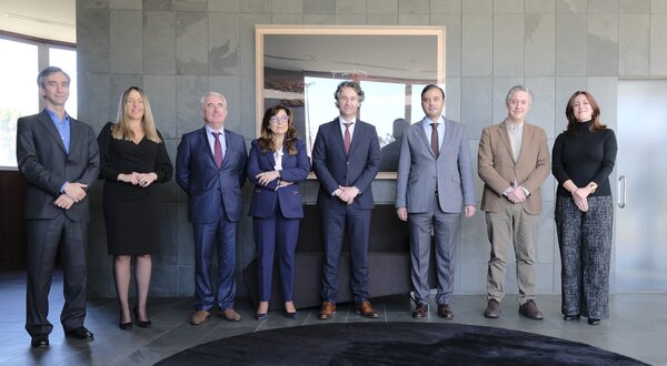 Grupo de oito pessoas em trajes formais, posando em ambiente moderno.