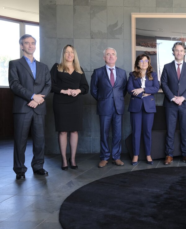 Grupo de oito pessoas em trajes formais, posando em ambiente moderno.