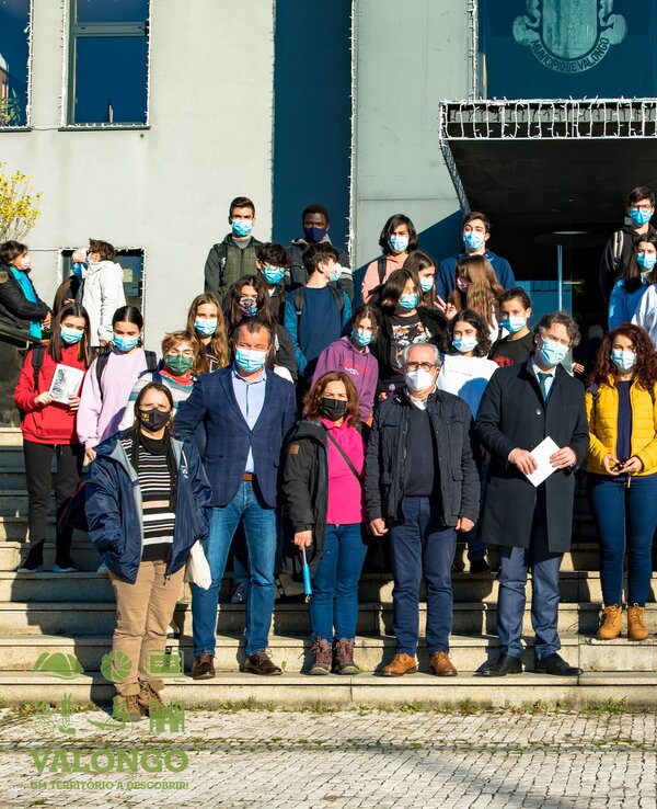 Grupo de estudantes e professores em frente a um edifício, todos com máscaras.