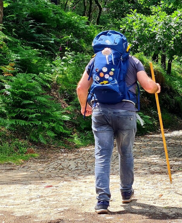 Homem a caminhar por um trilho florestal, com mochila e bastão.