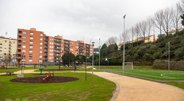 Parque com relvado, campo de futebol e edifícios residenciais ao fundo.