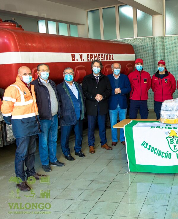 Grupo de bombeiros e autoridades em frente a um veículo, com bandeira da associação.