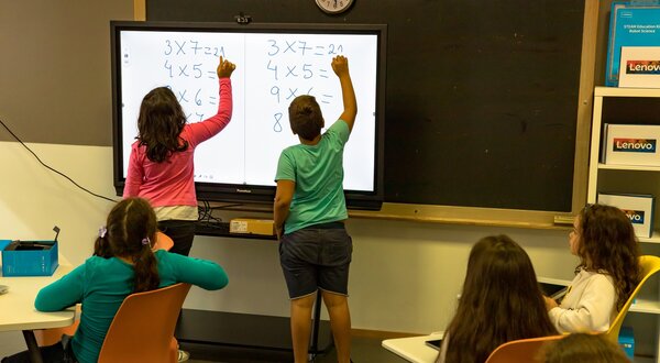 Crianças a resolver problemas de matemática num quadro interativo.