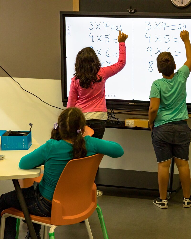 Crianças a resolver problemas de matemática num quadro interativo.
