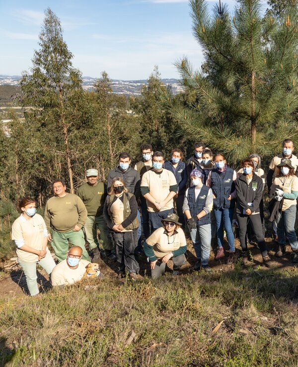 Grupo de pessoas em um bosque, todas usando máscaras, posando para a foto.