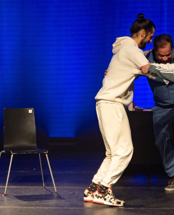 Três pessoas em cena, interagindo em um ambiente teatral iluminado.