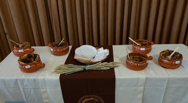 Mesa com pratos de barro cheios de comida, talheres e pratos brancos.