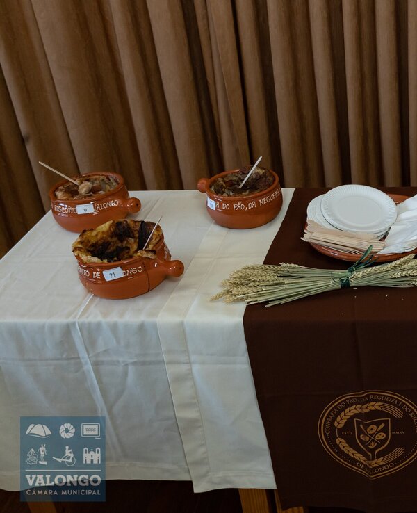 Mesa com pratos de barro cheios de comida, talheres e pratos brancos.