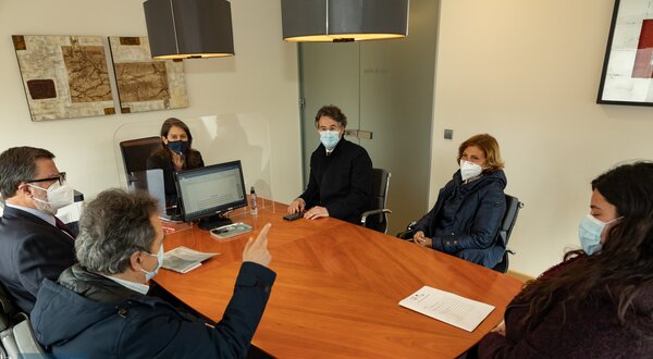 Reunião em sala com seis pessoas à volta de uma mesa de madeira.