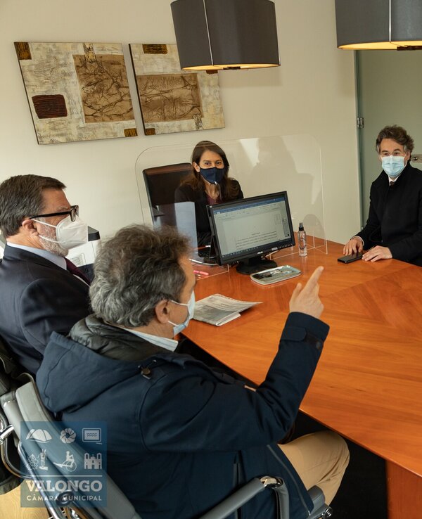 Reunião em sala com seis pessoas à volta de uma mesa de madeira.