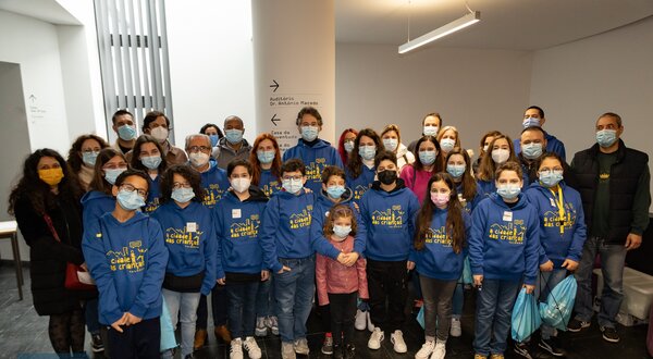 Grupo de pessoas com camisolas azuis em ambiente interior, algumas crianças à frente.