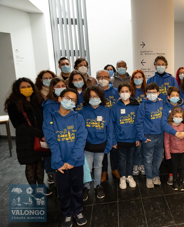 Grupo de pessoas com camisolas azuis em ambiente interior, algumas crianças à frente.