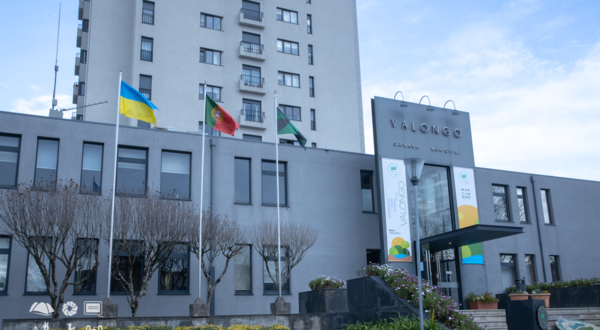 Fachada da Câmara Municipal de Valongo com bandeiras e jardim bem cuidado.