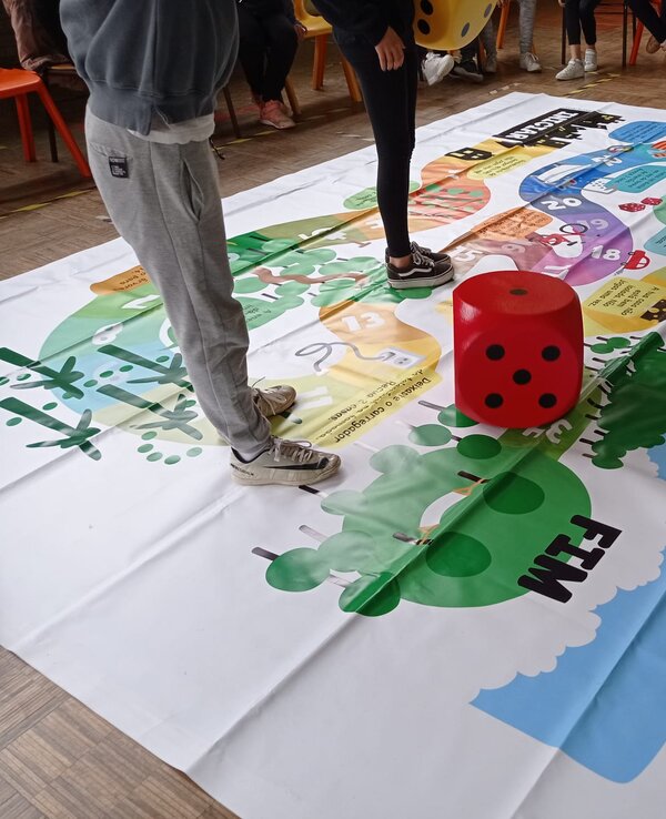 Um jogo de tabuleiro grande no chão, com um dado vermelho ao centro.