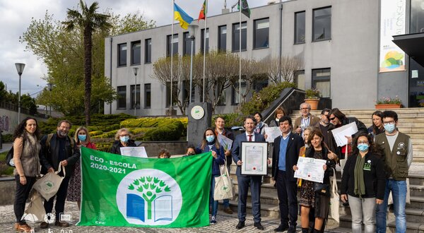 Grupo de pessoas com bandeira Eco-Escola em frente a um edifício.