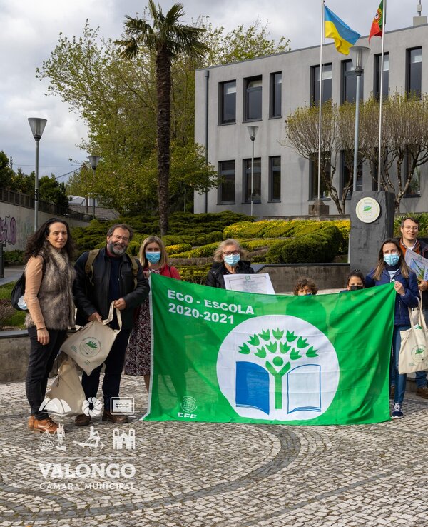 Grupo de pessoas com bandeira Eco-Escola em frente a um edifício.