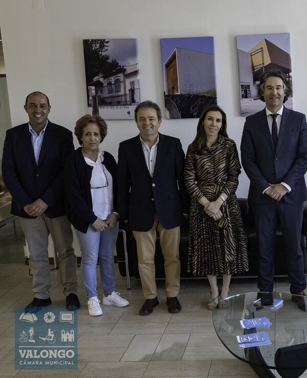 Grupo de pessoas em pé, posando em um ambiente com fotografias ao fundo.