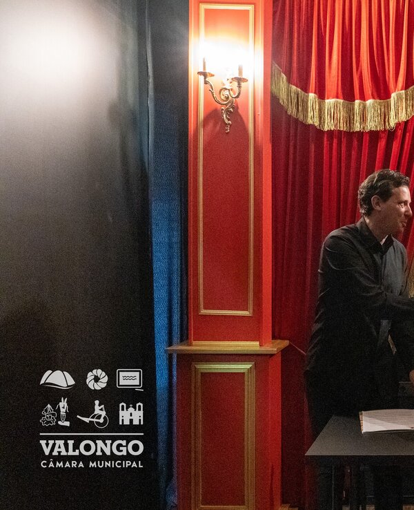 Duas pessoas a apertar as mãos em frente a um fundo de cortinas vermelhas.