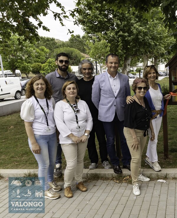 Grupo de pessoas posando junto a um pequeno abrigo para pássaros.