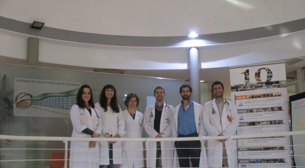 Seis profissionais de saúde em jalecos brancos, posando em um balcão.