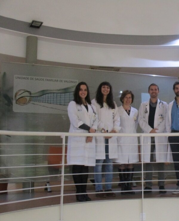 Seis profissionais de saúde em jalecos brancos, posando em um balcão.