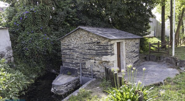 Casa de pedra junto a um ribeiro, rodeada de vegetação e flores.