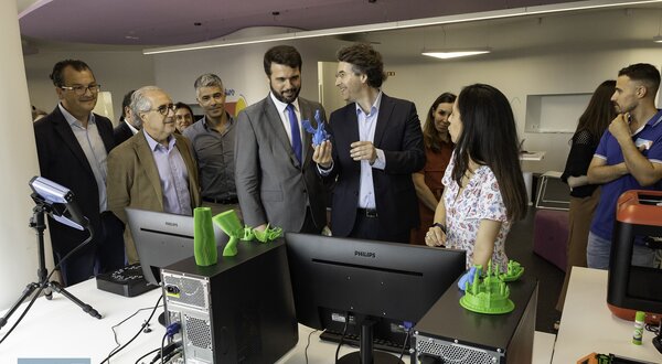 Grupo de pessoas a observar uma demonstração de impressão 3D em ambiente moderno.