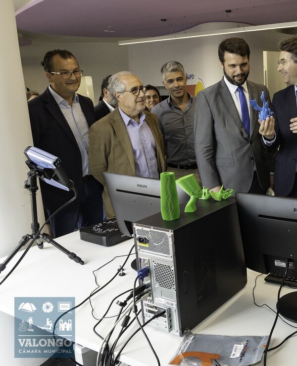 Grupo de pessoas a observar uma demonstração de impressão 3D em ambiente moderno.