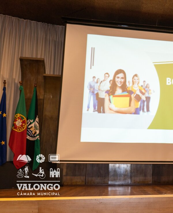 Homem a falar num palco sobre bolsas de estudo, com apresentação ao fundo.
