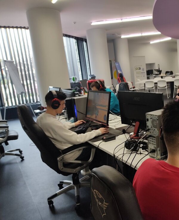 Quatro jovens a jogar videojogos em computadores num espaço moderno.