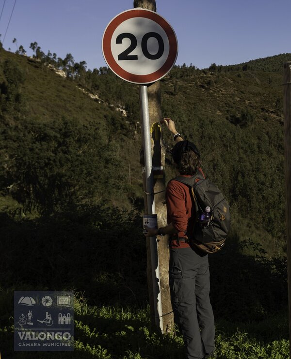 Pessoa a colocar um adesivo num sinal de limite de velocidade de 20 km/h.