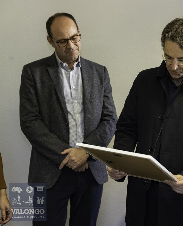 Três homens em um ambiente interno, observando um quadro.