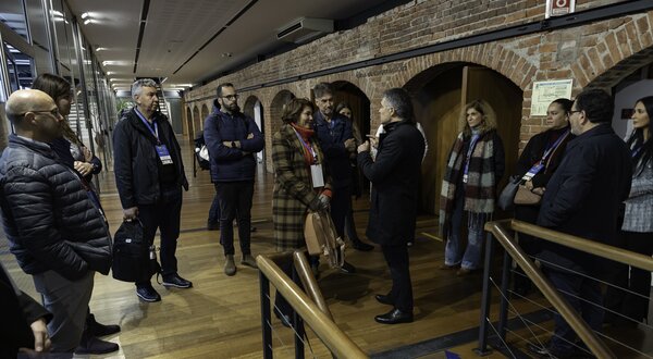 Grupo de pessoas em visita guiada num espaço com paredes de tijolo exposto.
