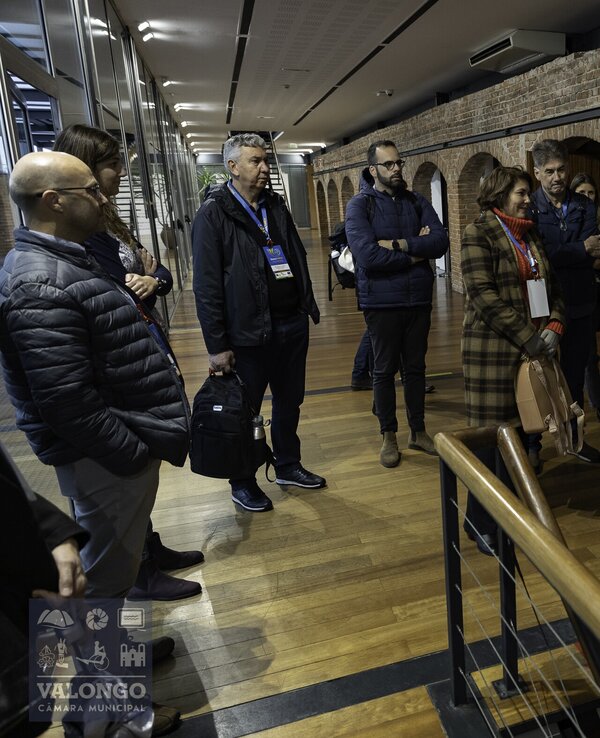 Grupo de pessoas em visita guiada num espaço com paredes de tijolo exposto.
