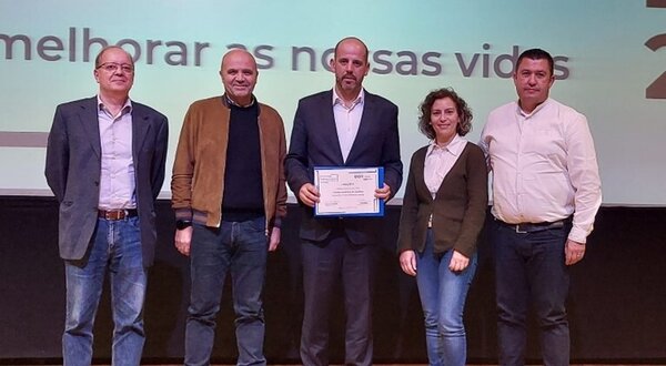 Grupo de cinco pessoas em palco, segurando um certificado de reconhecimento.