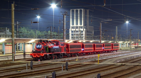 Locomotiva antiga iluminada à noite, com vagões decorados em luzes.