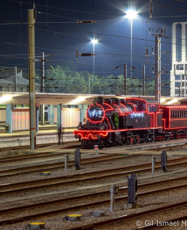 Locomotiva antiga iluminada à noite, com vagões decorados em luzes.
