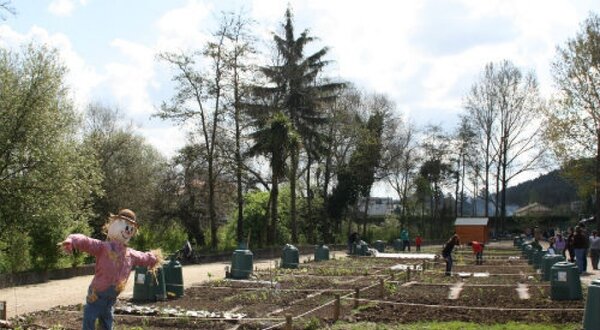 Um campo com um espantalho, árvores e pessoas a trabalhar na horta.