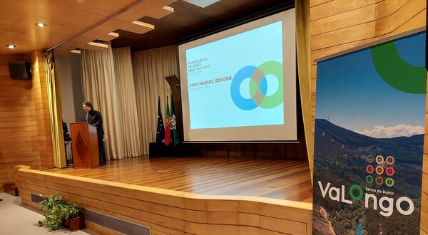 Um orador em palco, com apresentação sobre Valongo ao fundo.